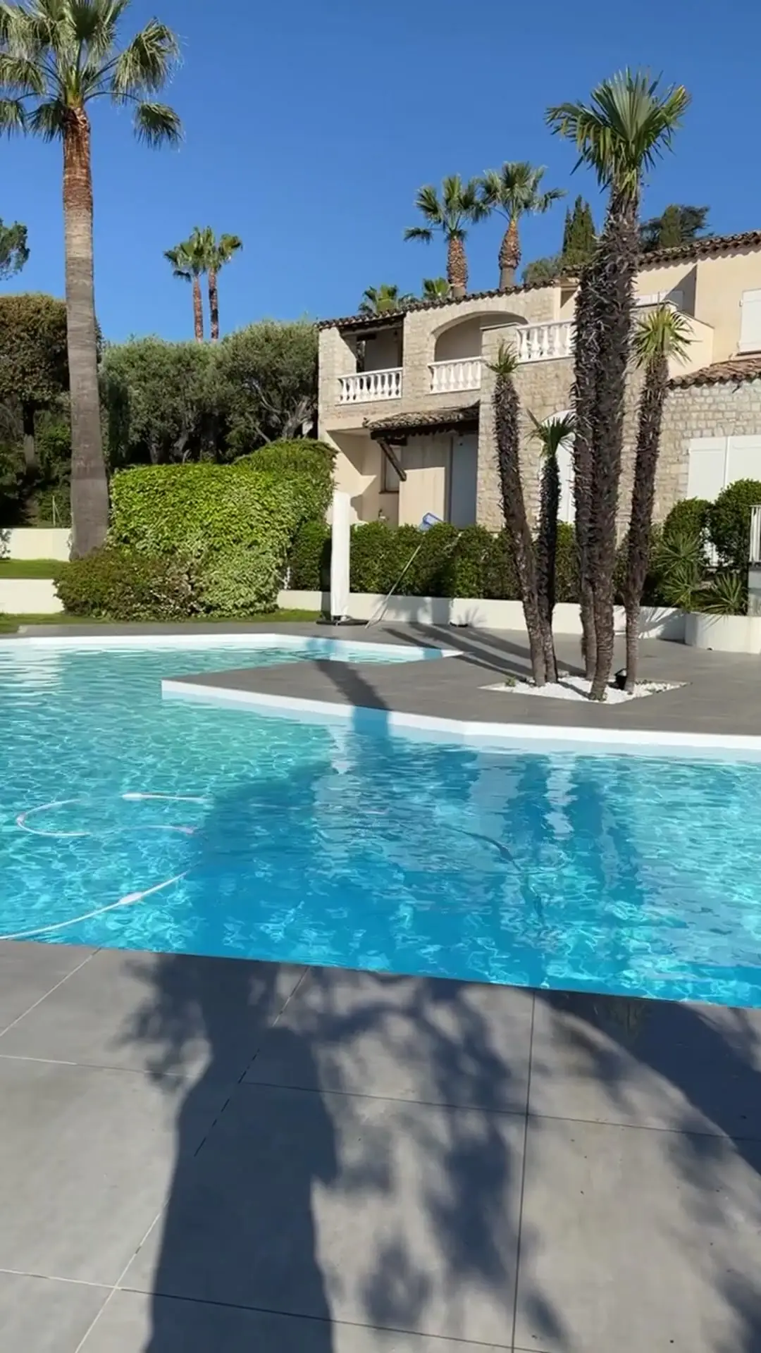 Piscine blanche bordée de palmiers devant une villa en pierre